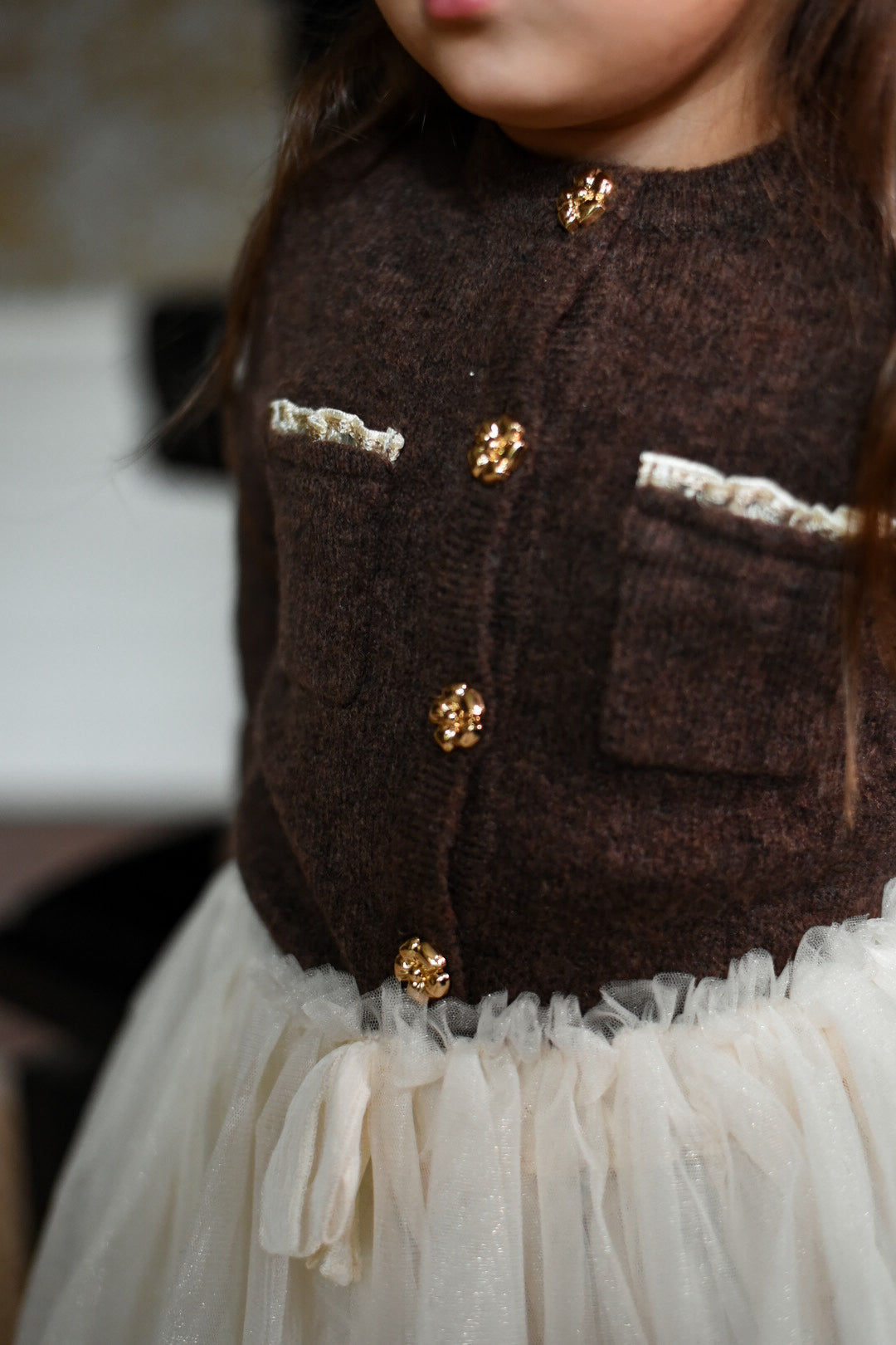 Detail of the Charlie Knit Cardigan in Chocolate with gold flower buttons and ivory trim in the Canal House