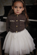 Girl wearing the Charlie Knit Cardigan in Chocolate with the Julie Tutu Skirt in White beside a piano in the Canal House