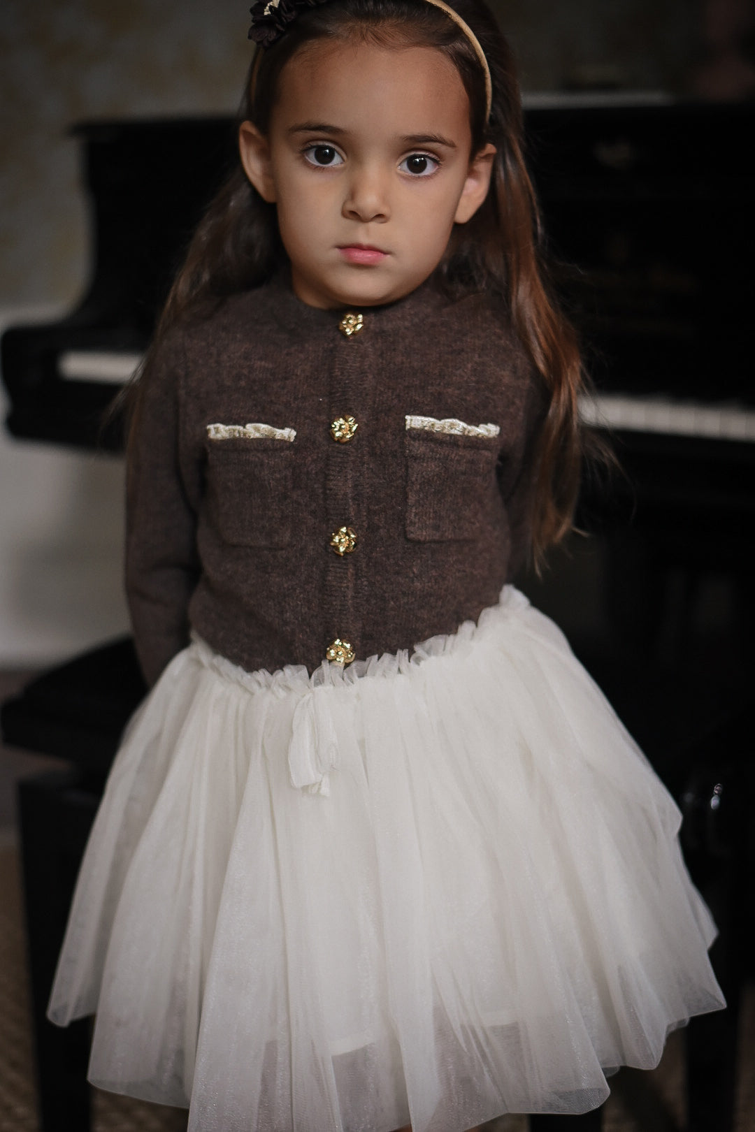 Girl wearing the Charlie Knit Cardigan in Chocolate with the Julie Tutu Skirt in White beside a piano in the Canal House