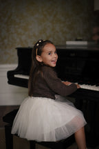 Girl wearing the Charlie Knit Cardigan in Chocolate with the Julie Tutu Skirt in White at the piano in the Canal House
