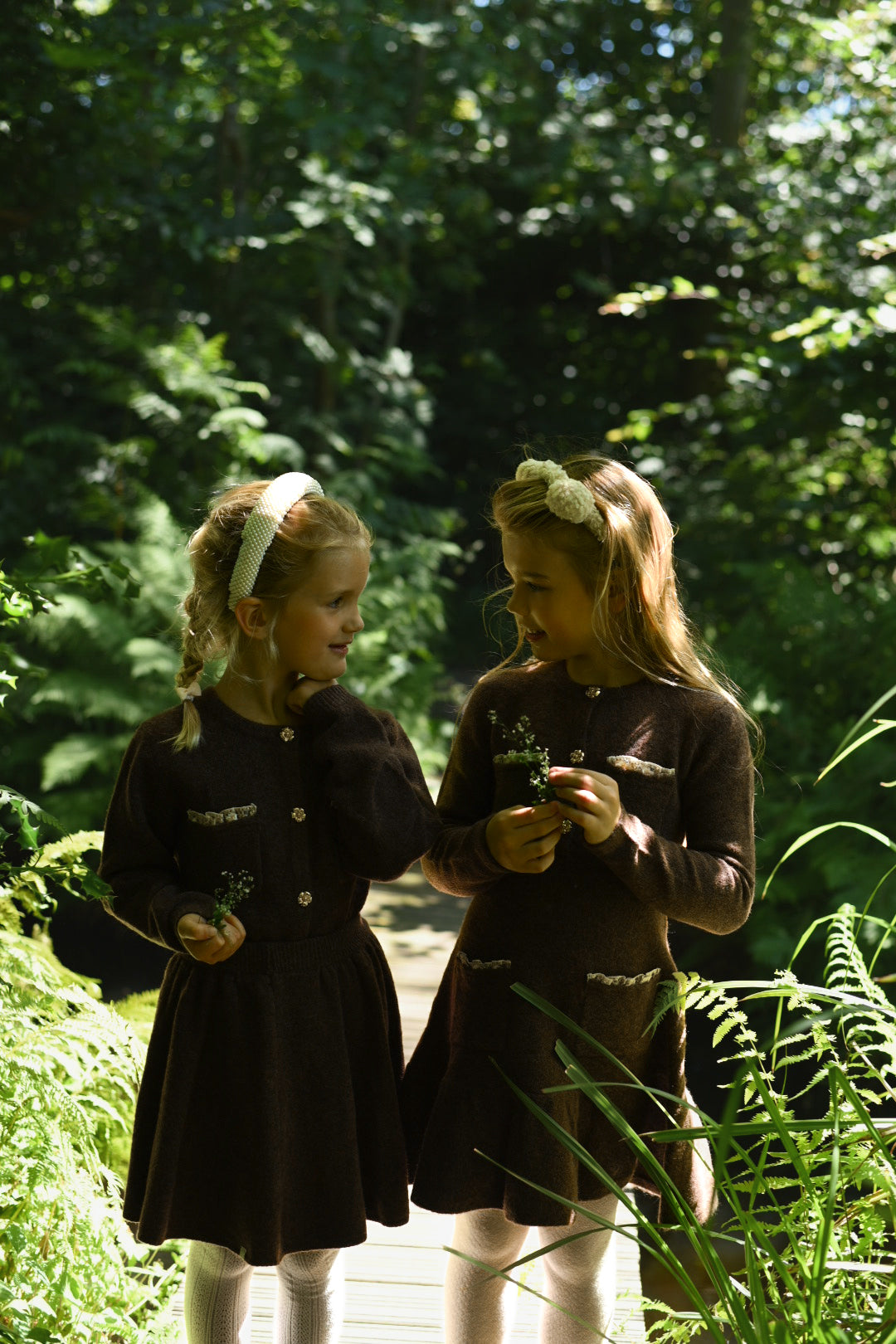 Two girls wearing chocolate and ivory LRDM Petits dresses in the woodland