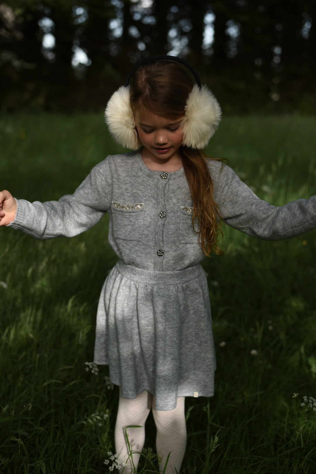 Girl wearing the dove Charlie Knit cardigan and skirt among woodland flowers