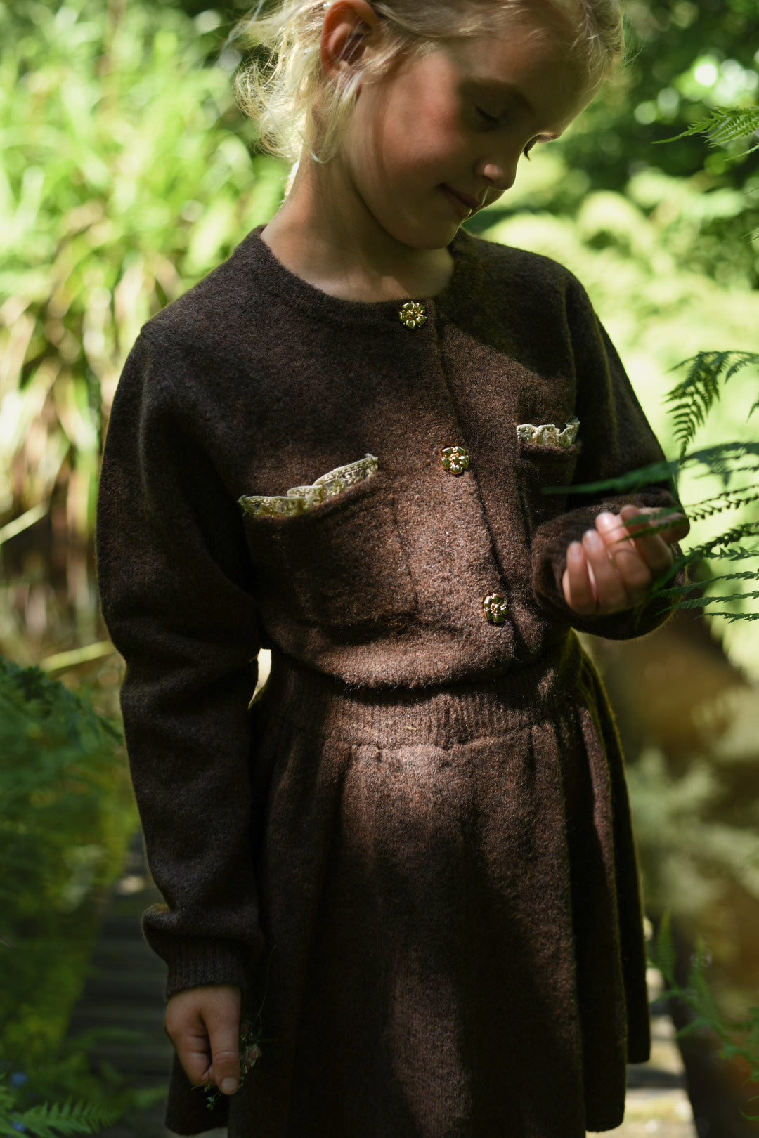 Girl wearing the chocolate Charlie Knit cardigan and matching skirt among woodland ferns