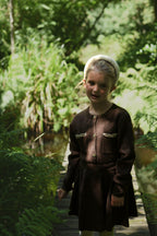 Girl wearing the chocolate Charlie Knit cardigan and matching skirt in the woodland