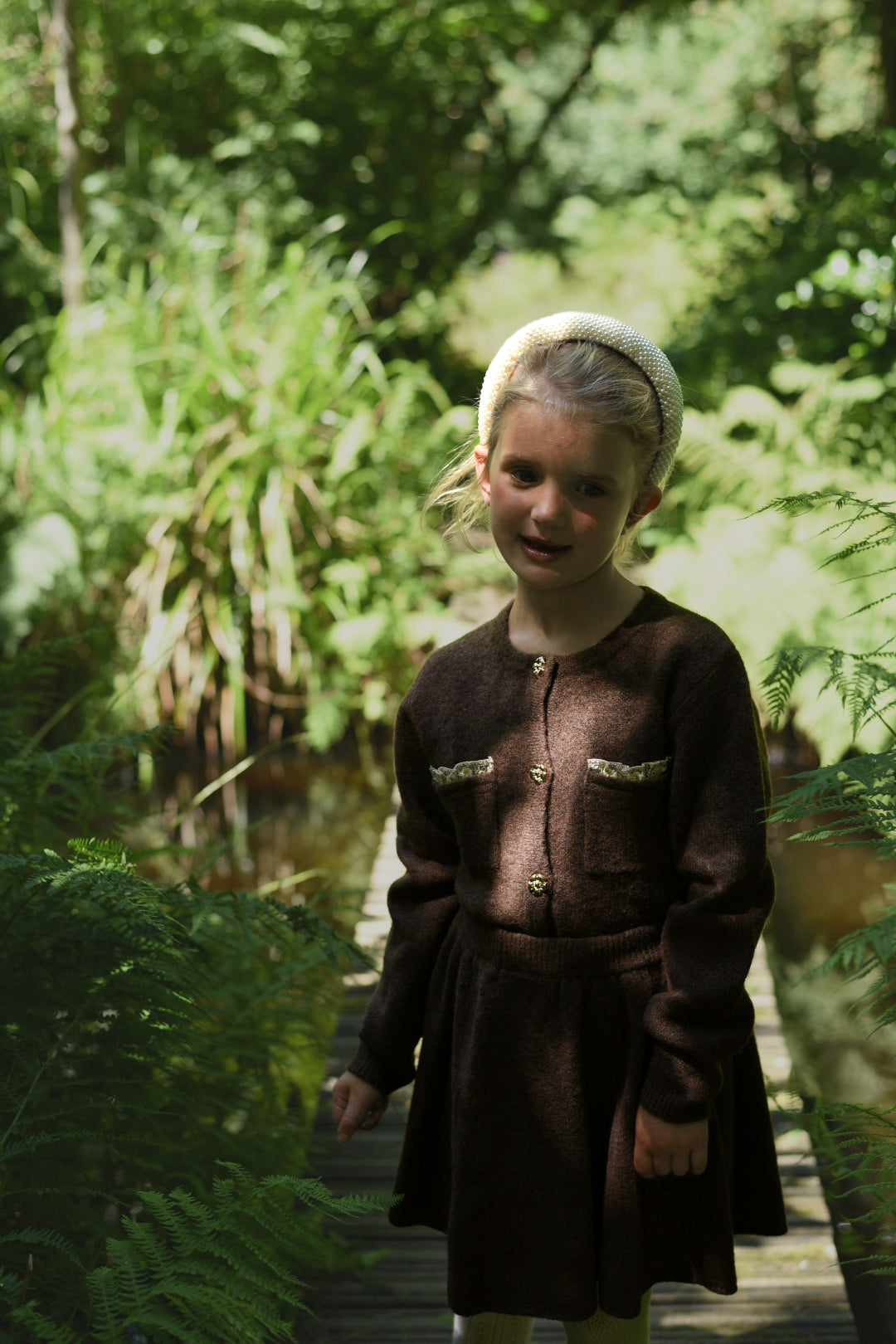 Girl wearing the chocolate Charlie Knit cardigan and matching skirt in the woodland