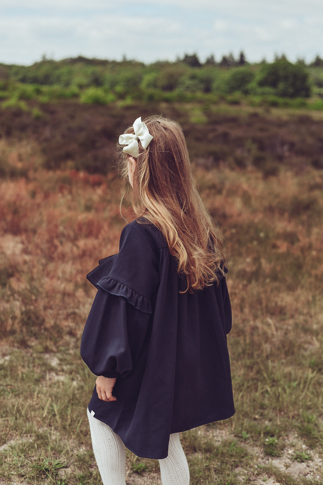 Back view of a girl wearing the Elle Dress in Navy on the heath