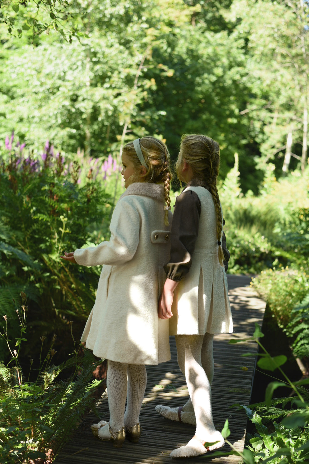 Two girls wearing ivory Mara Tweed coats in the woodland