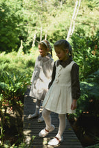 Side view of girls wearing ivory Mara Tweed looks in the woodland
