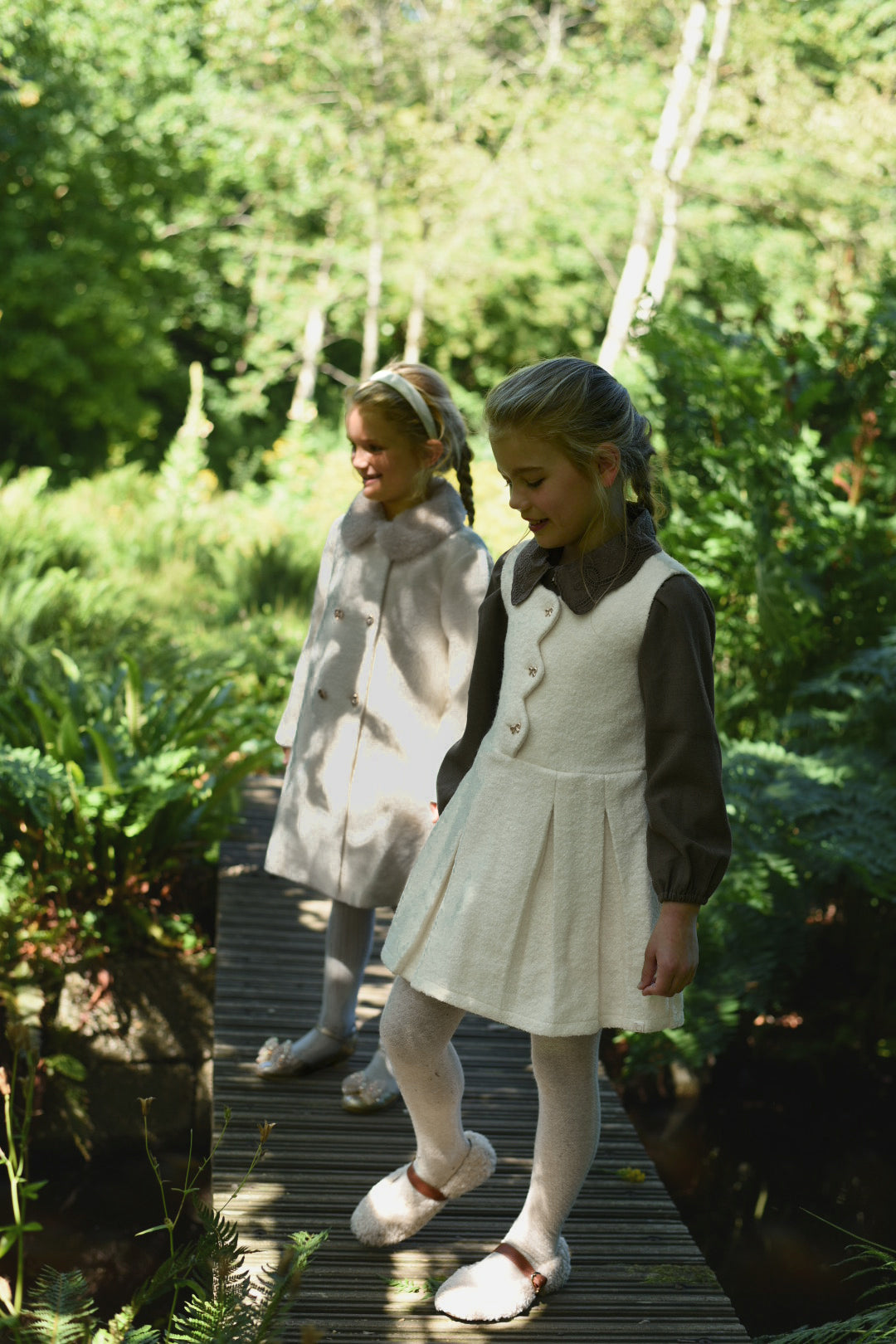 Side view of girls wearing ivory Mara Tweed looks in the woodland