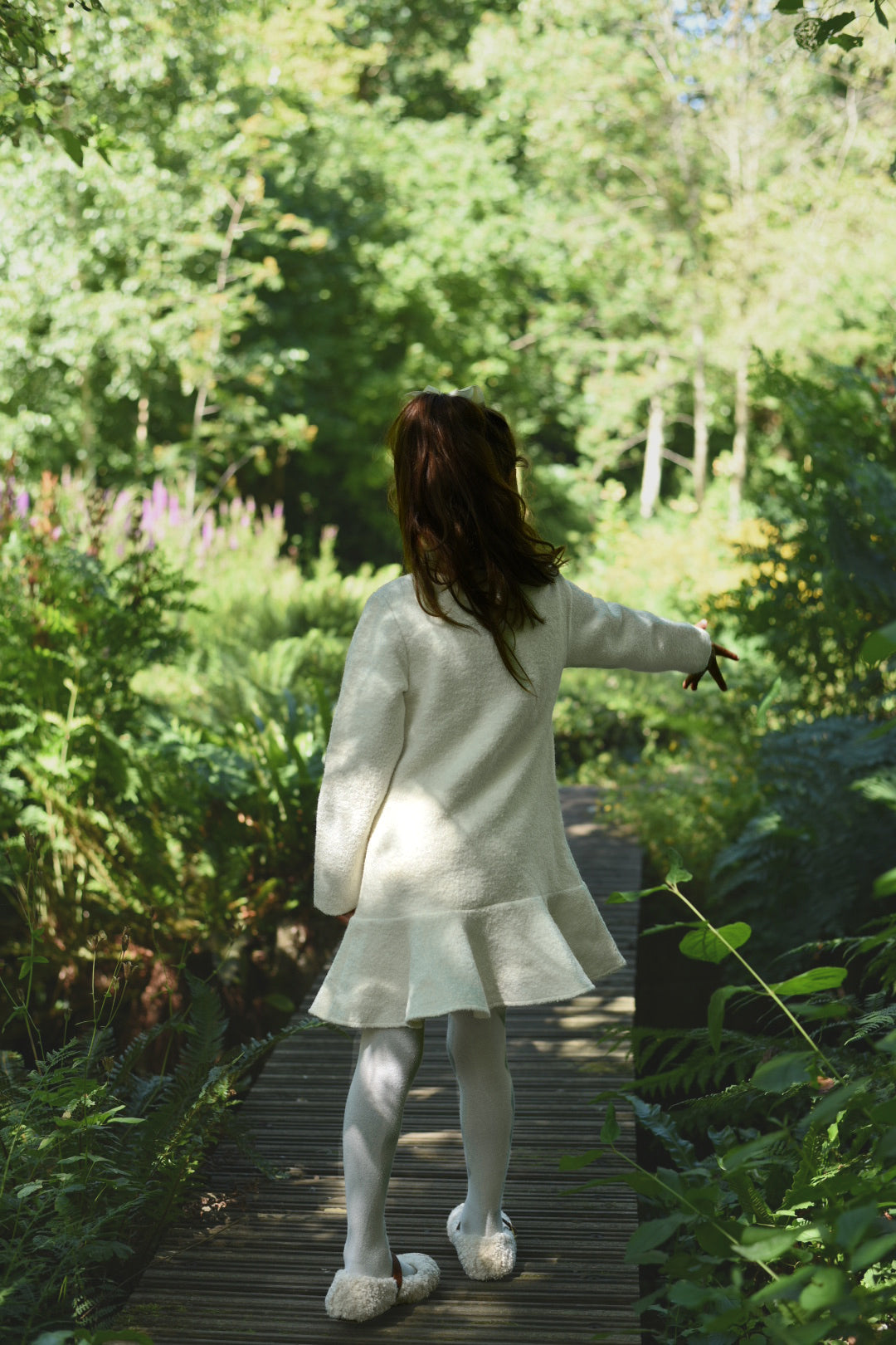 Back view of a girl wearing the long-sleeve Mara Tweed Dress in the woodland