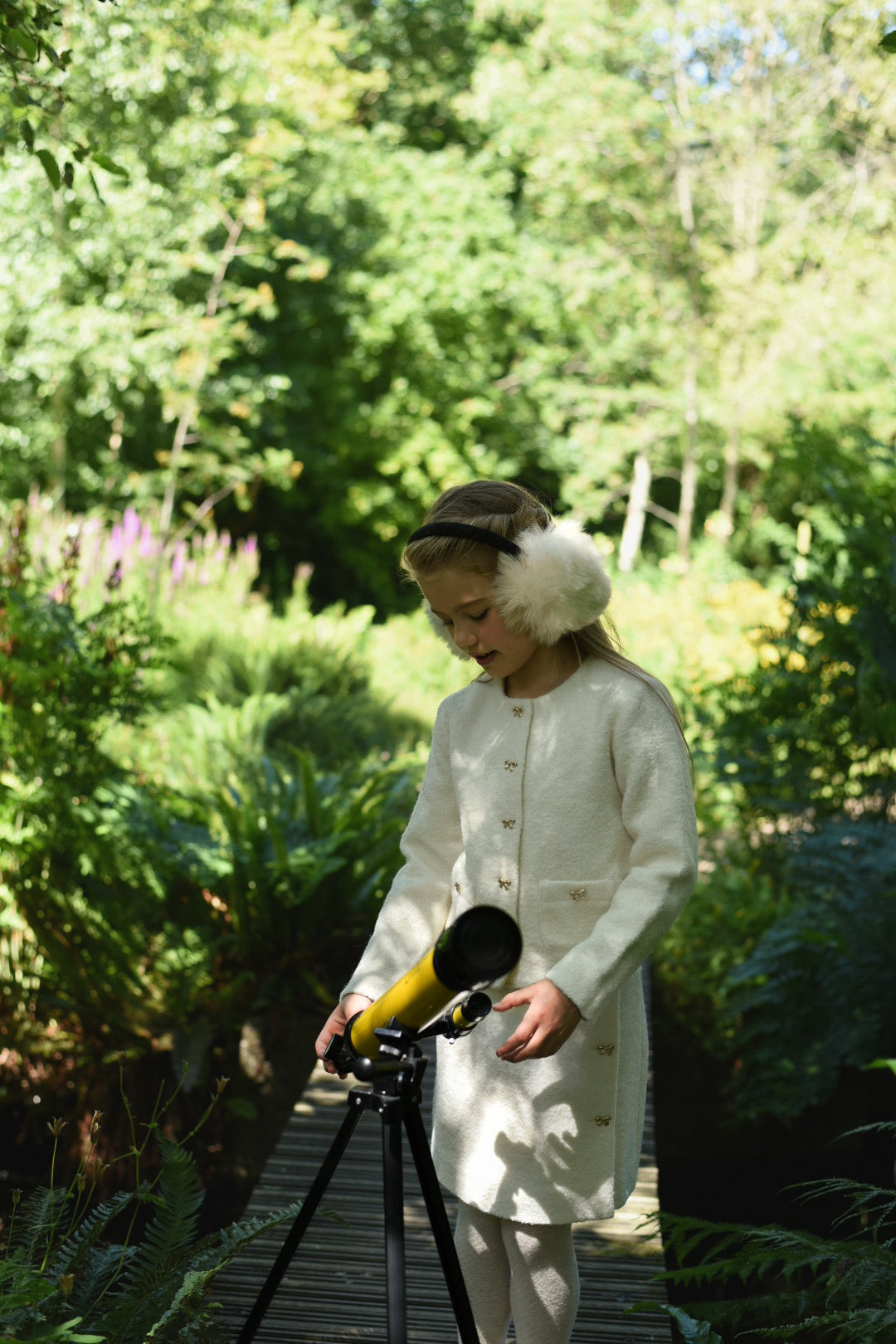Girl wearing the Mara Tweed Jacket and matching skirt while looking through a telescope in the woodland
