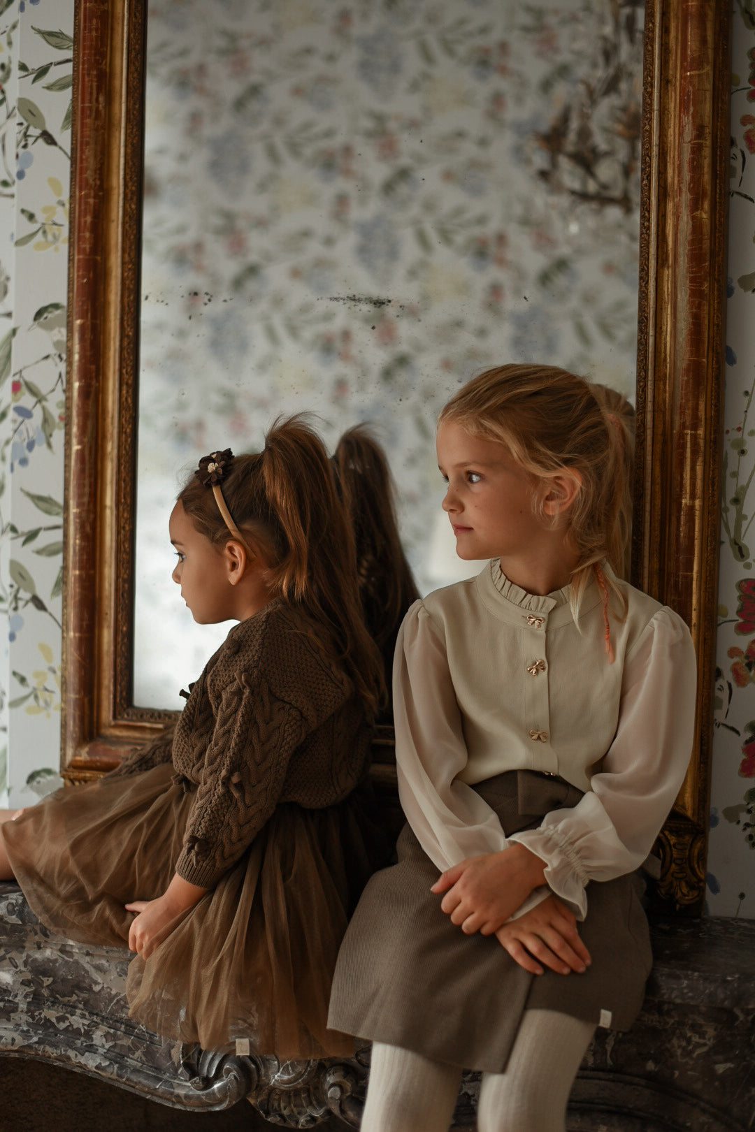Girl wearing the Zara Blouse in sand seated beside an antique mirror in the Canal House