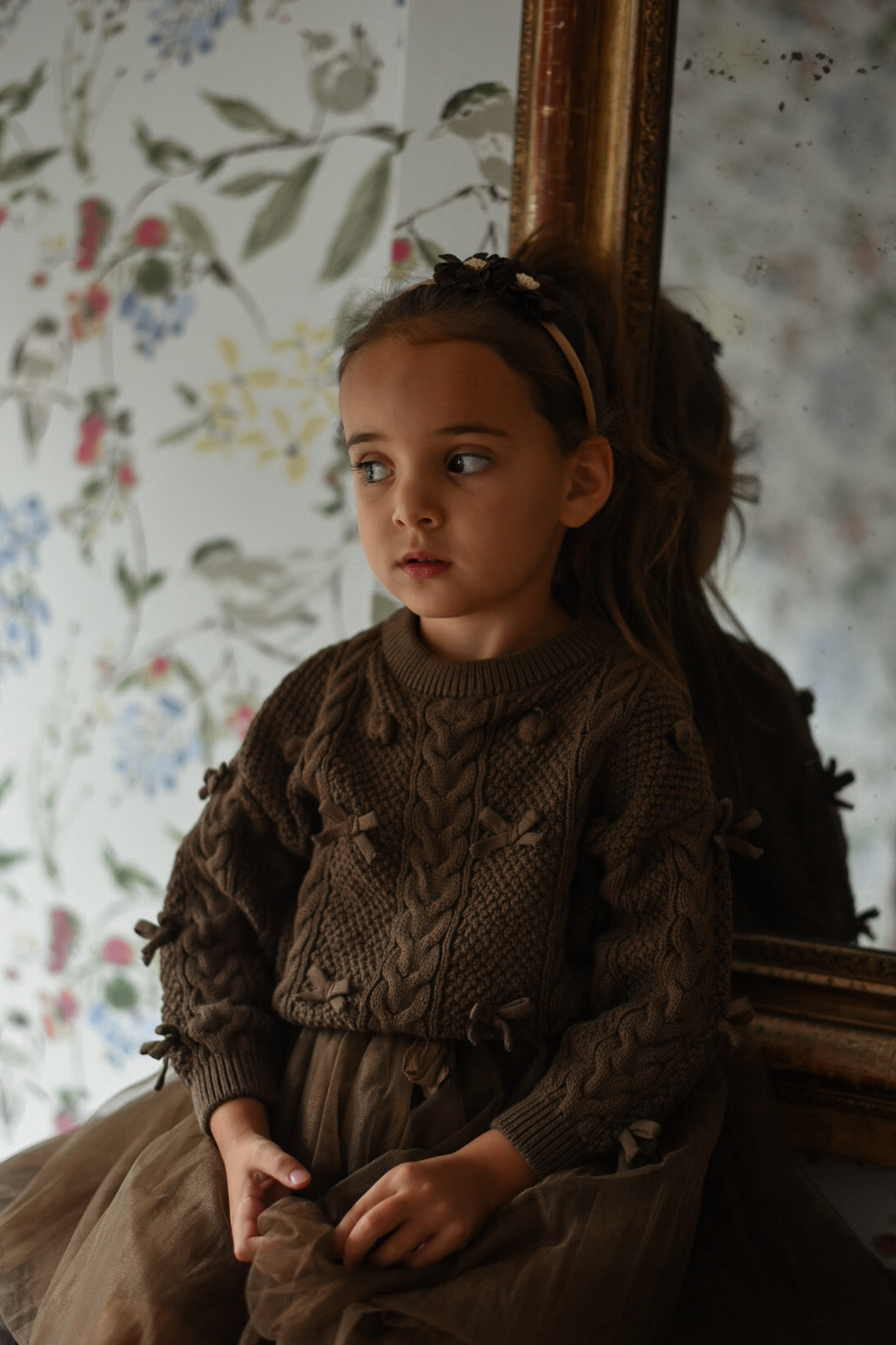 Girl wearing the Elise Bow Pull in chocolate beside an antique mirror in the canal house