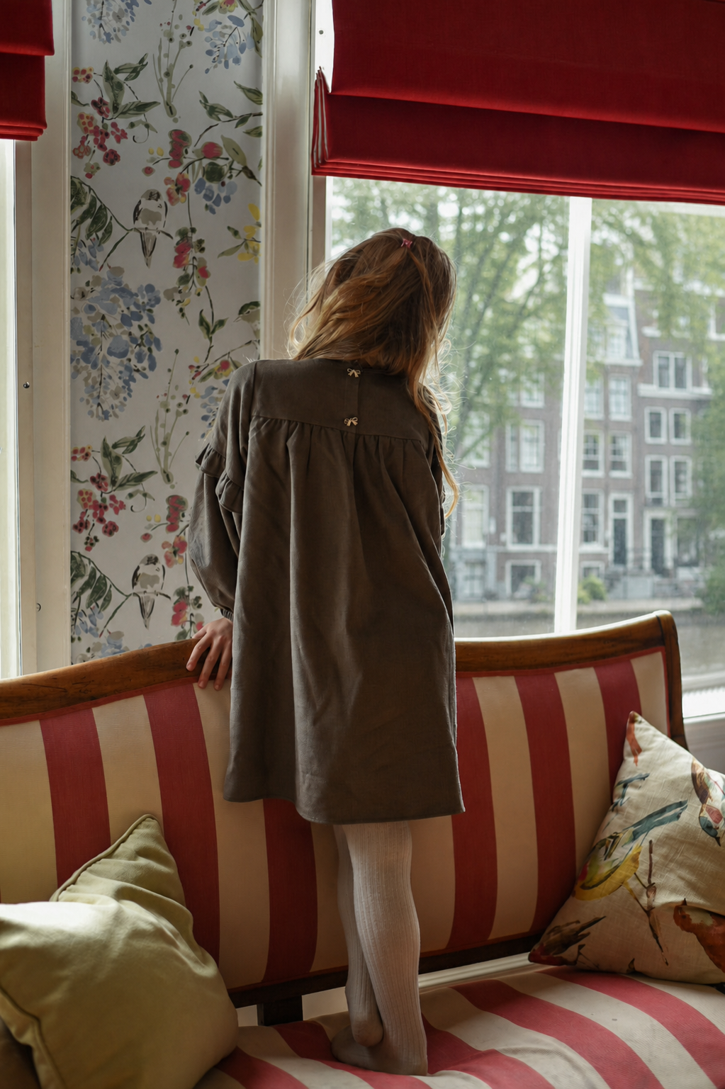 Back view of the Elle Dress in chocolate with bow buttons by the Canal House windows