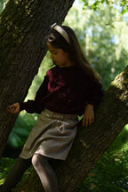 A girl wearing the Isabella Skirt in quiet check with burgundy knitwear in the forest