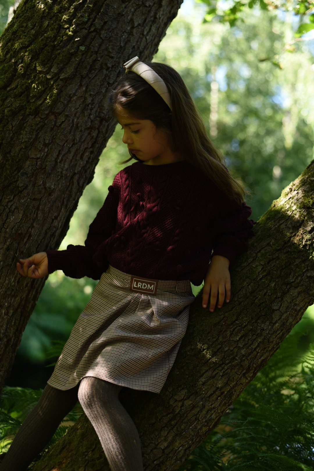 A girl wearing the Isabella Skirt in quiet check with burgundy knitwear in the forest