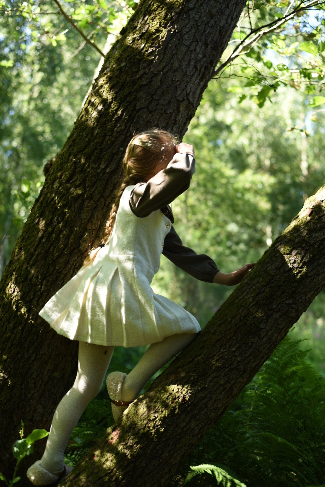 A girl playing beside a tree in an LRDM Petits AW26 woodland look