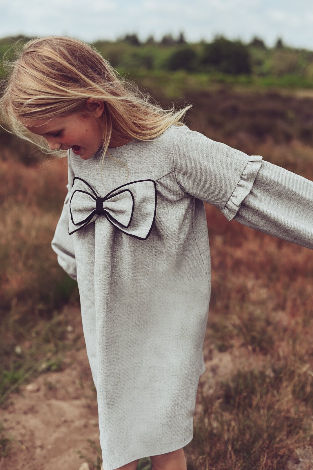 A girl wearing the Elle Dress in dove with a statement bow