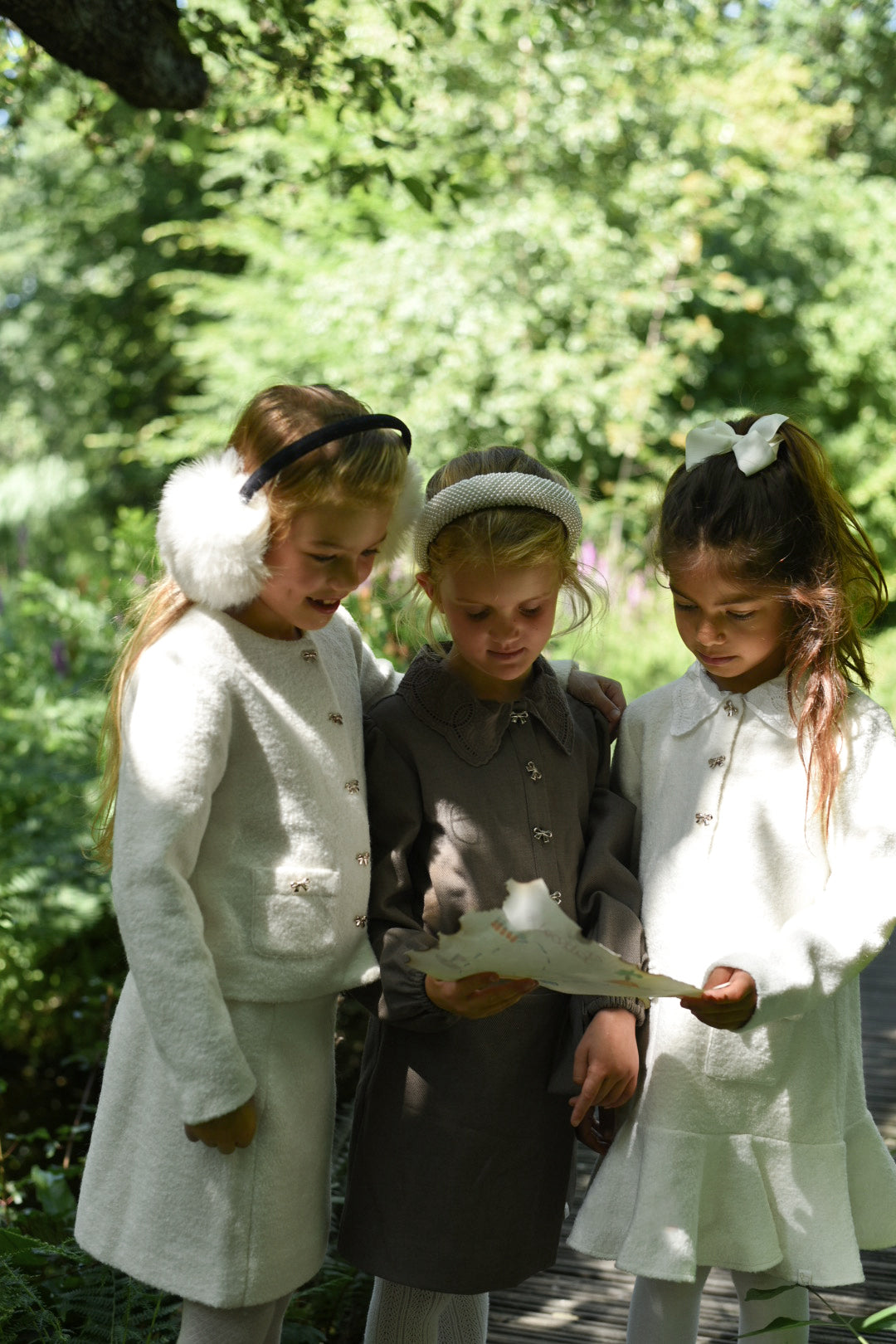 Three girls in LRDM Petits AW26 looks discovering a map together in woodland light